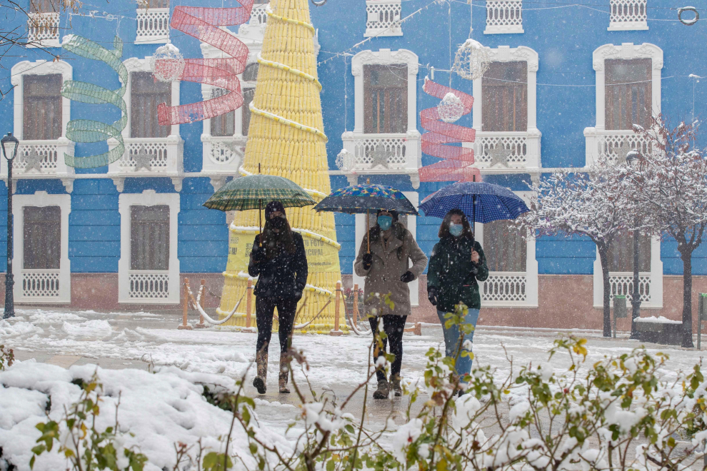 Tres jóvenes se protegen de la nieve con paraguas este jueves por la plaza del ayuntamiento de Bullas, Murcia.