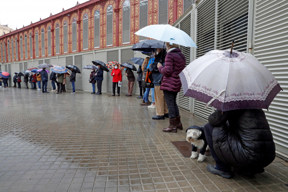 Varios votantes hacen cola, bajo la lluvia, en uno de los colegios electorales del Mercat de Sant Antoni de Barcelona a primera hora de este domingo.