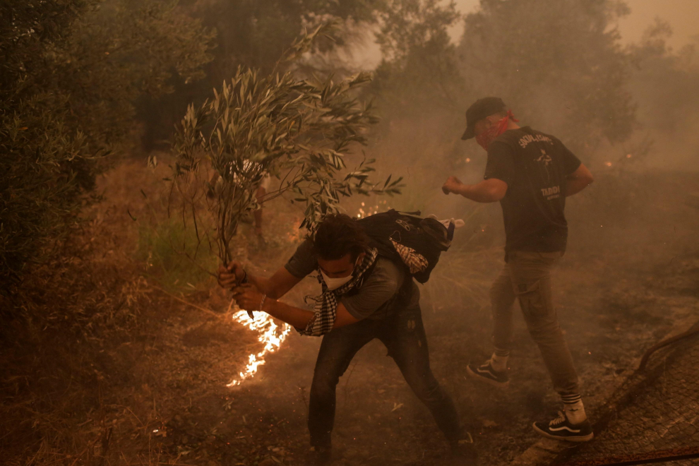 Los vecinos de Pefki tratan de apagar las llamas locales usan una rama de árbol para combatir en la isla de Evia,