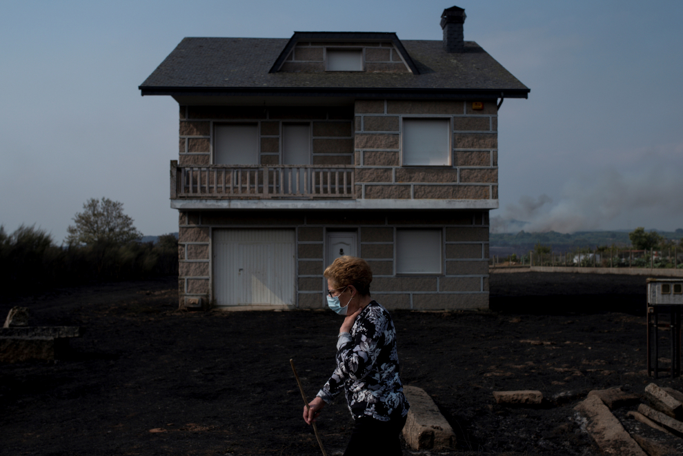 Una mujer camina junto a una vivienda afectada por el fuego en la localidad de Carzoá (Cualedro).