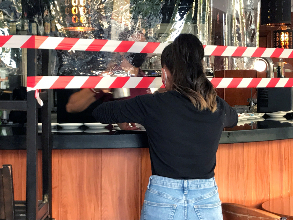 Una camarera se prepara para llevar el pedido a una mesa delante de las cintas que advierten de que la barra de la cafetería del hostal Don Pedro, al lado de hospital Gomez Ulla, en el barrio de Vista Alegre, ha sido clausurada este lunes como medida de prevención contra el coronavirus.