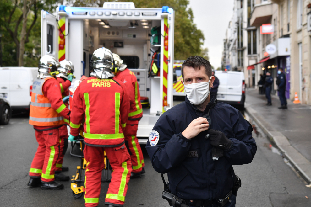 Un oficial de policía hace guardia mientras los bomberos suben a una persona lesionada a una ambulancia. Al menos cuatro personas han resultado heridas en un ataque con cuchillo cerca de la antigua redacción de la revista satírica "Charlie Hebdo".