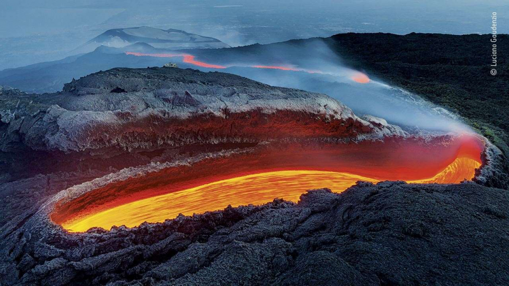 La lava fluía de una gran abertura en el lado del volcán, corría a lo largo de un enorme túnel y resurgía más abajo en la ladera como un río rojo incandescente.