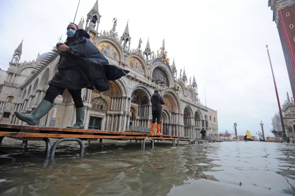 Un hombre camina sobre un puente mientras las mareas altas golpean Venecia.