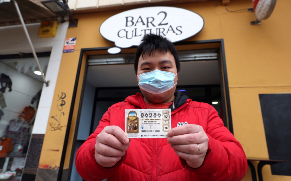 Juan, propietario del bar Dos Culturas de Zaragoza, muestra uno de los décimos agraciados con el quinto premio 86986 del Sorteo Extraordinario de Lotería de Navidad.