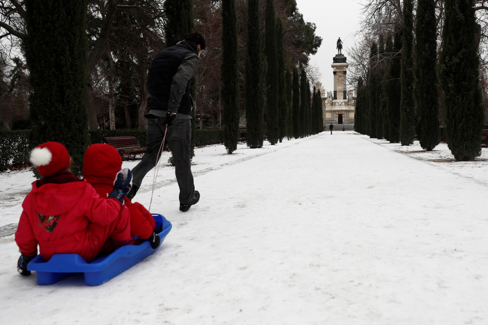 Un hombre tira de un trineo con niños sobre el manto de nieve que cubre el parque del Retiro.