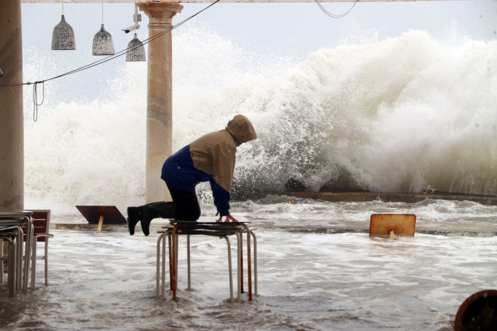 Una persona subida a una mesa del mobiliario de una terraza ante las inundaciones por la borrasca Filomena en Málaga.