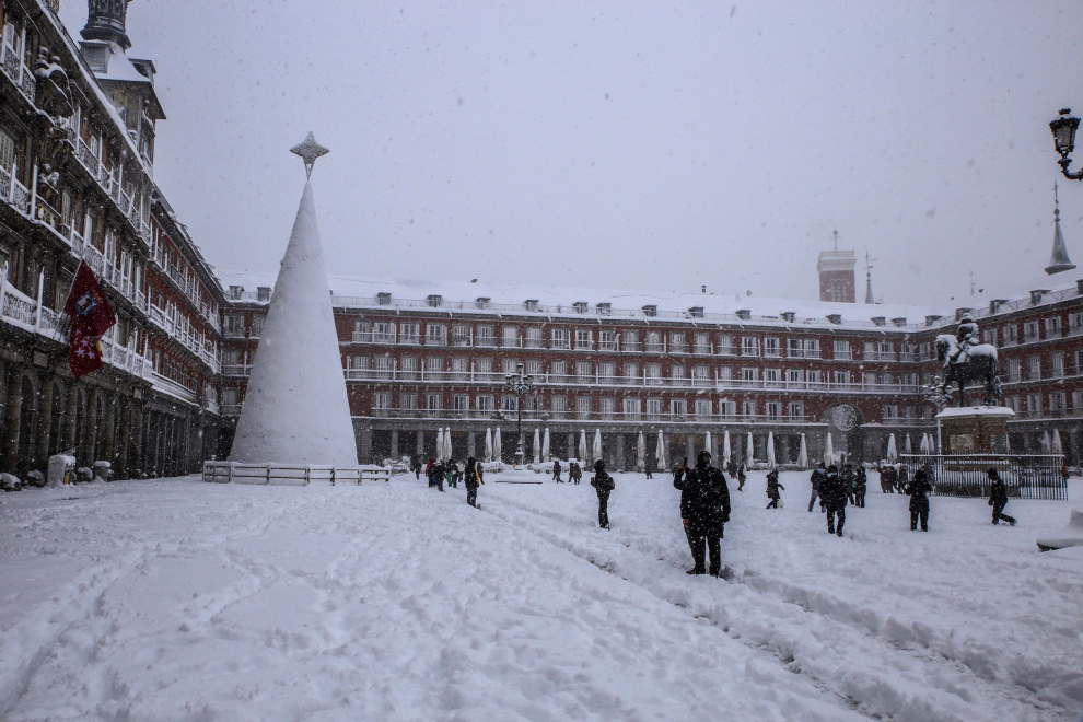 Varias personas caminan bajo la nieve en la Plaza Mayor de Madrid