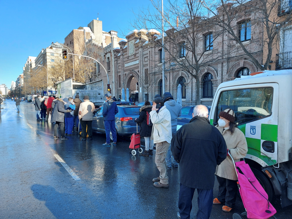 Varias personas hacen cola en la calle Santa Engracia de Madrid, que se encuentra despejada de la nieve gracias a los esparcidores de sal y salmuera que se están distribuyendo en la capital.