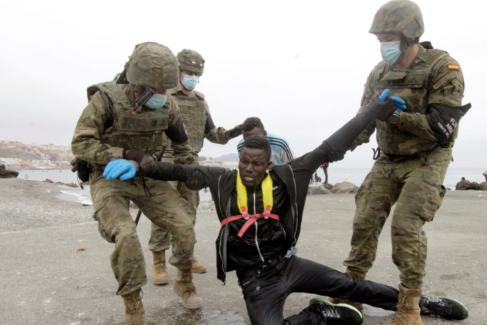 Miembros del Ejército de Tierra ayudan a un inmigrante que han logrado cruzar uno de los espigones fronterizos de Ceuta