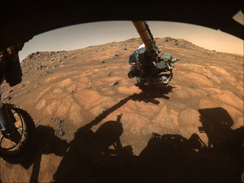El brazo robótico del rover Perseverance extiende la mano para examinar rocas en un área de Marte apodada el área "Cratered Floor Fractured Rough". Los científicos están interesados ​​en las rocas planas que parecen de color claro.