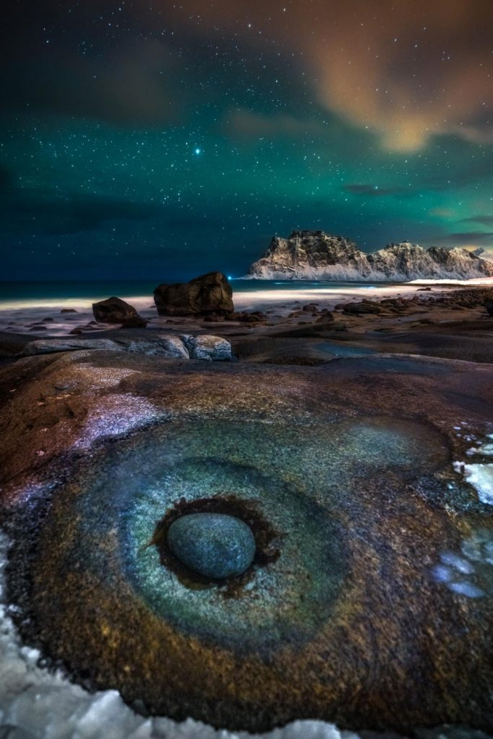 Ganadora categoría Cielo Nocturno. En la playa de Uttakleiv, en Noruega, estas rocas en particular parecían un ojo. La toma se contrasta con los hermosos colores de la aurora boreal de arriba.