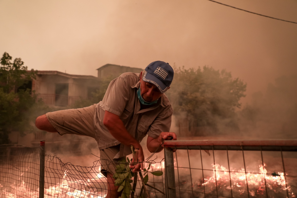Un hombre salta una valla para escapar de las llamas durante un incendio forestal en la aldea de Pefki en la isla de Evia, a unos 189 kilómetros al norte de Atenas.