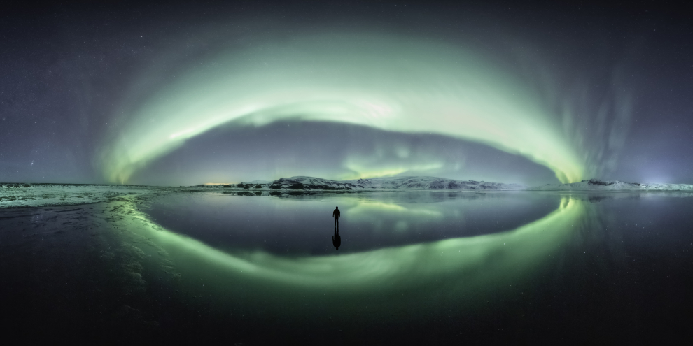 Este es un panorama de 250 de las auroras boreales en Islandia. El fotógrafo encontró este estuario que reflejaba el cielo perfectamente en una noche de inviernos muy por debajo de la congelación, y capturó el panorama primero, y luego tomó una foto de sí mismo en el hielo. Vik, Región Sur, Islandia, 31 de enero de 2020