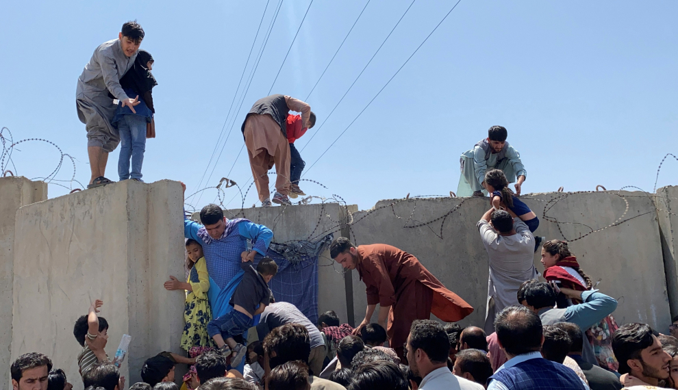 Afganos se agolpan a lo largo del muro del aeropuerto internacional Hamid Karzai en Kabul, Afganistán, el 16 de agosto de 2021, para saltar el muro en un intento de poder abandonar el país después de darse a conocer que el propio presidente afgano, Ashra Ghani había huido del país después de que los talibanes tomaran control de la capital.