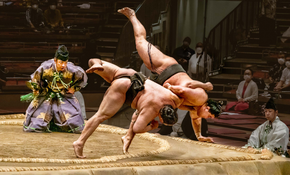 Dos luchadores de sumo intentan hacer tropezar uno al otro fuera del ring en una fracción de segundo.