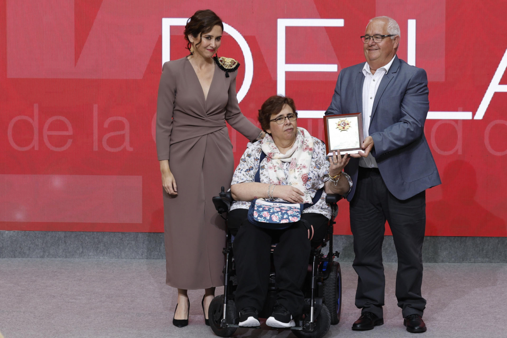 La presidenta de la Comunidad de Madrid, Isabel Díaz Ayuso (i), entrega uno de los galardones al obrero de la construcción Jacinto Tapusa (d), que lo recoge acompañado de su esposa Remedios Pérez