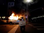 Un manifestante muestra una pancarta mientras arde una furgoneta de la Policía de Nueva York a su espalda