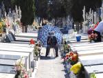 Una mujer aguarda protegida del sol, mientras un familiar arregla una lápida, en el Cementerio de Nuestro Padre Jesús de Murcia