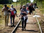 Migrantes y refugiados caminan con sus hijos por la vía del tren en la frontera de Hungría