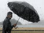 Un hombre se protege de la lluvia con una paraguas mientras pasea junto a la bahía de La Concha de San Sebastián. (Juan Herrero / EFE)