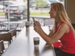 Una mujer toma café mientras mira el móvil