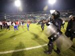 Aficionados ingresan al campo y se protegen de los gases lacrimógenos lanzados por las autoridades, debido a los disturbios a las afueras del Estadio Nacional por la cancelación del clásico entre Olimpia y Motagua hoy sábado, en Tegucigalpa. Al menos tres