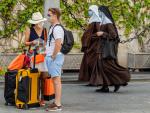 Dos turistas esperan en la calle mientras pasan dos monjas; todos ellos, con mascarilla