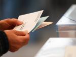 Una persona sostiene papeletas electorales frente a las urnas