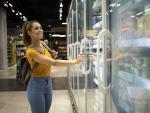 Una chica abre la nevera de los helados en un supermercado