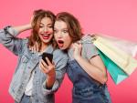 shocked-two-women-friends-holding-shopping-bags-using-mobile-phone