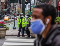 Un ciudadano con mascarilla pasa por delante de varios policías en Nueva York.