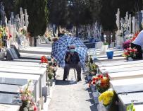 Una mujer aguarda protegida del sol, mientras un familiar arregla una lápida, en el Cementerio de Nuestro Padre Jesús de Murcia.
