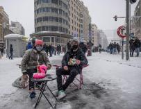Dos personas se sientan en una nevada Plaza de Callao de Madrid tras el paso de Filomena.