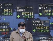 Un inversor consulta su móvil ante un panel de la Bolsa de Tokio.