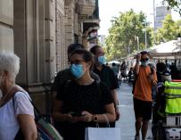 Decenas de personas protegidas con mascarilla hacen cola para entrar en una biblioteca, en Barcelona