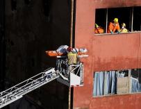 Los Bomberos sacan por la ventana de la nave uno de los cuerpos de las tres víctimas del incendio