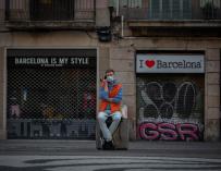 Un hombre se sienta delante de varios comercios turísticos cerrados en Barcelona.