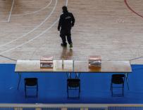 Un trabajador coloca varias urnas en una mesa electoral situada en un complejo deportivo.