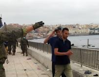 Un miembro del Ejército de Tierra da instrucciones a un grupo de inmigrantes en uno de los espigones fronterizos de Ceuta