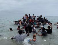 Un grupo de personas se hacen con una embarcación de las autoridades marroquíes en la playa de la localidad de Fnideq (Castillejos) para cruzar los espigones de Ceuta, el 18 de mayo de 2021, en una avalancha de inmigrantes sin precedentes en España al registrarse la entrada en 24 horas de 5.000 personas (un tercio de ellas menores).