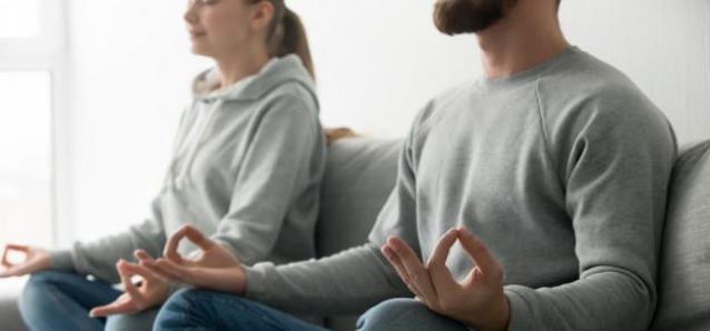 Una pareja practicando ejercicios de relajación y meditación en casa.