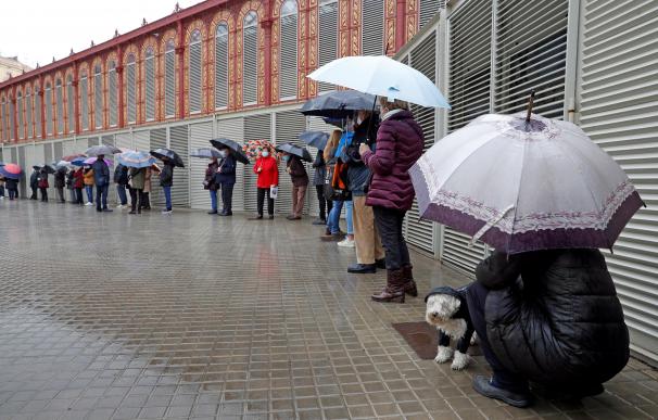 Varios votantes hacen cola, bajo la lluvia, en uno de los colegios electorales del Mercat de Sant Antoni de Barcelona a primera hora de este domingo.