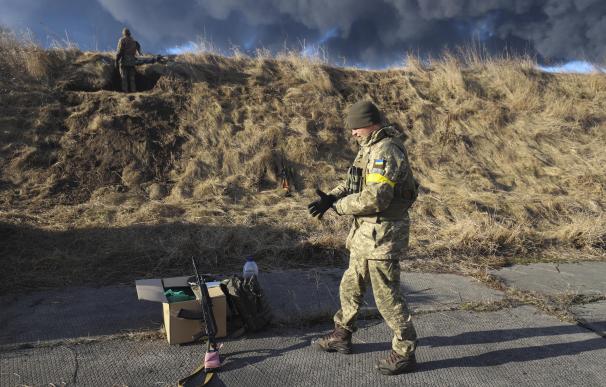 militares ucranianos descansan en una posición mirando el humo de un depósito de almacenamiento de petróleo quemado detrás después de que un misil ruso atacara cerca de Kiev, Ucrania, el 27 de febrero de 2022.