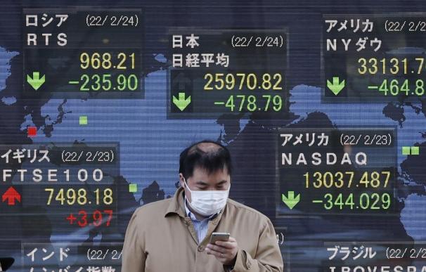 Un inversor consulta su móvil ante un panel de la Bolsa de Tokio.