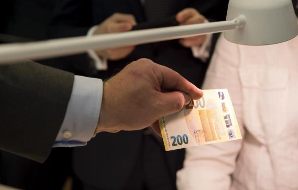 Un inversor observa un billete de 200 euros al trasluz.