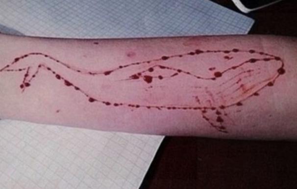 Una ballena tatuada en un brazo con un cuchillo