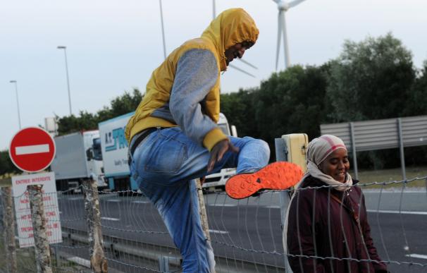 Un inmigrante trepa por la valla en Calais, cerca del Eurotúnel