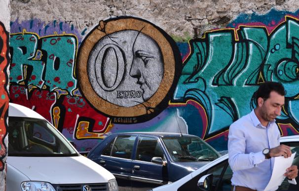 Un hombre camina delante de un graffiti que pone '0 euros' en Atenas
