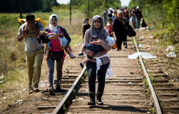 Migrantes y refugiados caminan con sus hijos por la vía del tren en la frontera de Hungría
